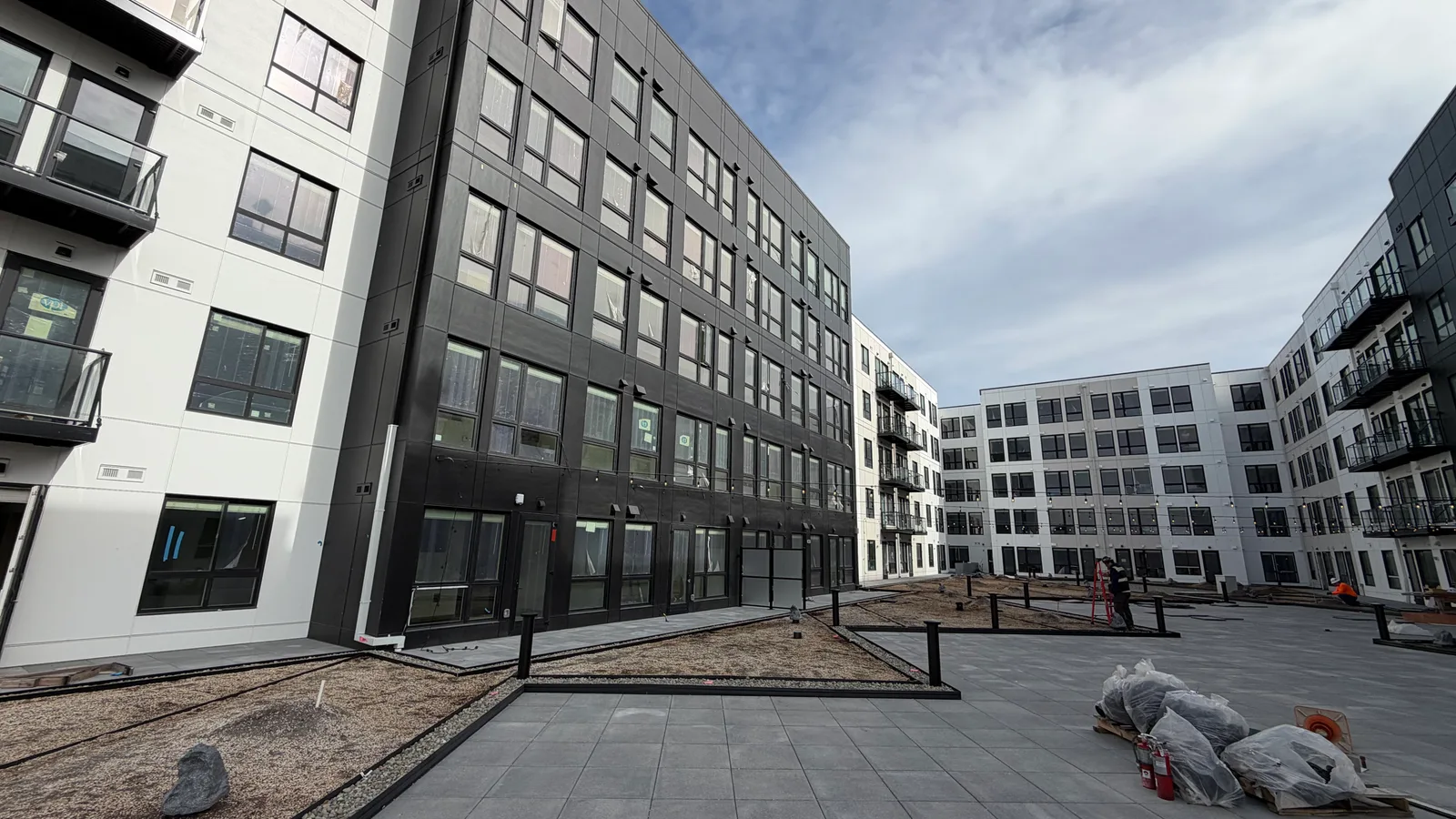 The courtyard at Cymbaluk Apartments: six-storey walls in white and charcoal panels with black balconies, new pavers and gravel beds in the foreground, and the far wings wrapping around the open space.