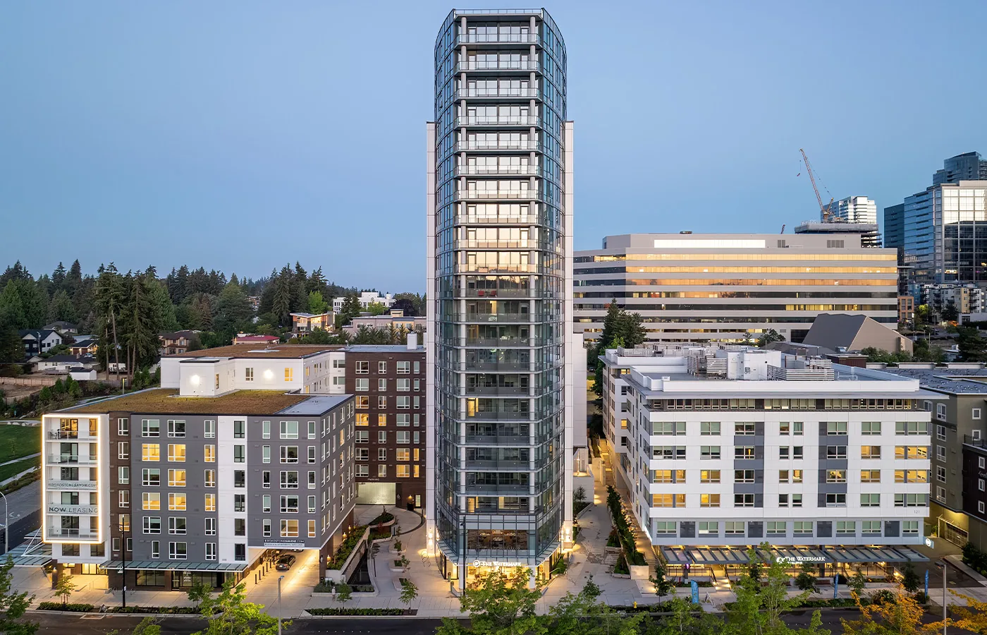 Holden, a retirement community in Bellevue, at dusk: a glass residential tower between two mid-rise buildings, windows lit, with downtown Bellevue office towers behind.